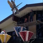 ARTIST REACHES FOR DRAGONFLY BEING LOWERED BY CRANE.